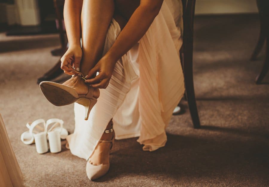 A bridesmaid sits on a chair and fastens a buckle on her new wedding shoes