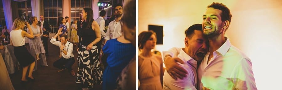 Wedding guests dancing and the groom and the best man hug each other on the dance floor