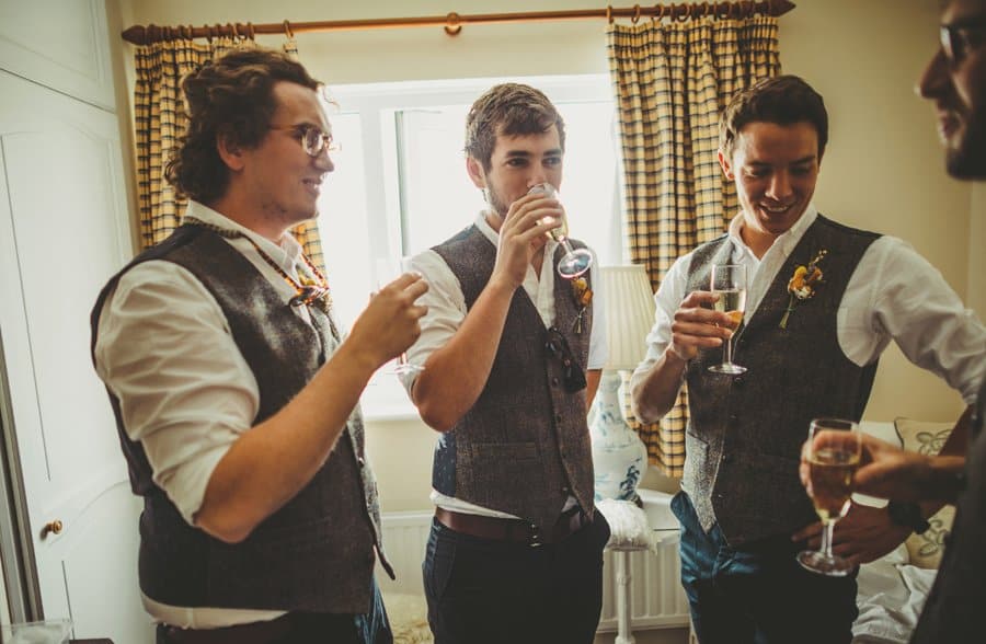 The groom and ushers stand together and sip champagne