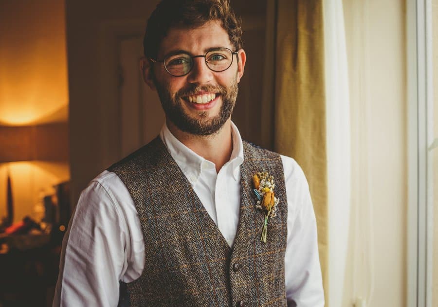 A portrait of the best man next to the window of the grooms parents house