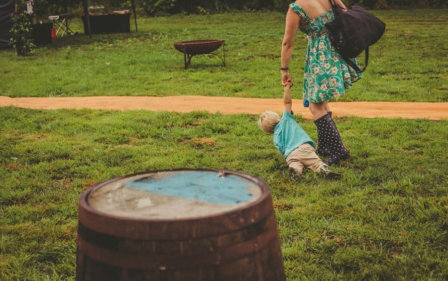 A little boy falls onto the grass whilst still holding his mothers hand