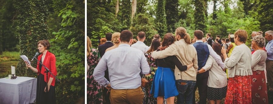 Wedding guests stand and listen to the outdoor wedding ceremony in the woods