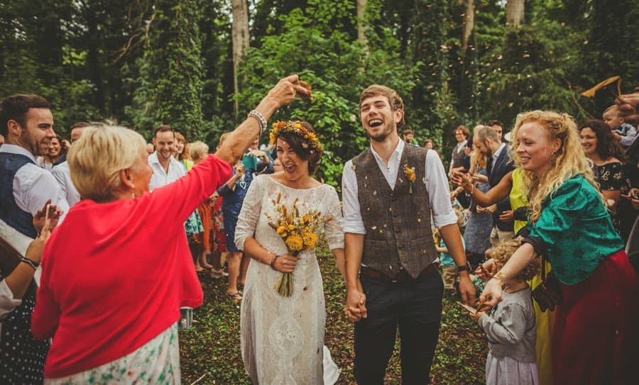 Confetti is thrown over the bride and groom as they walk out of the woods