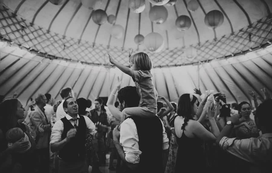 A child waves his arms in the air whilst sitting on his fathers shoulders on the dancefloor