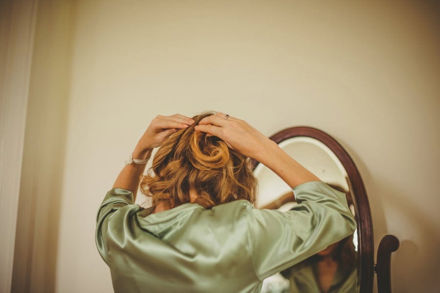 A bridesmaid fastens the back of her hair as she looks in the mirror