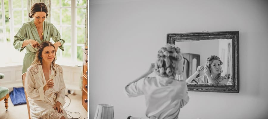 The bride sits on a chair and sips champagne and a bridesmaid takes rollers out of her as she looks in the mirror