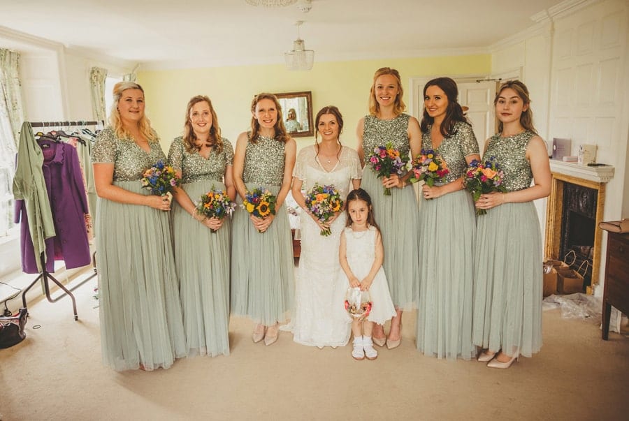 The bride, bridesmaids and flower girl pose for a photograph in the main bedroom at Barley Wood house