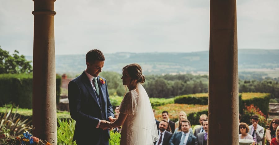The groom looks down on the floor and holds the brides hands during the outdoor ceremony