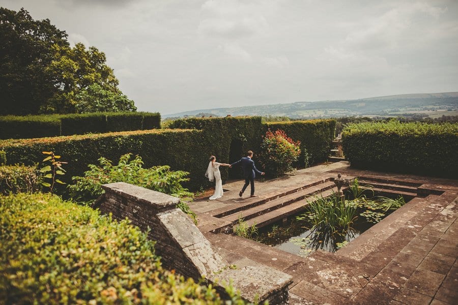 The bride and groom walk away from the wedding guests and outstretch their arms