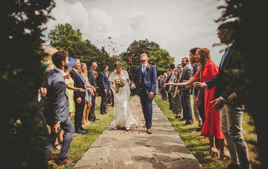 The groom holding the brides hand lifts his head in the air as confetti falls onto his face