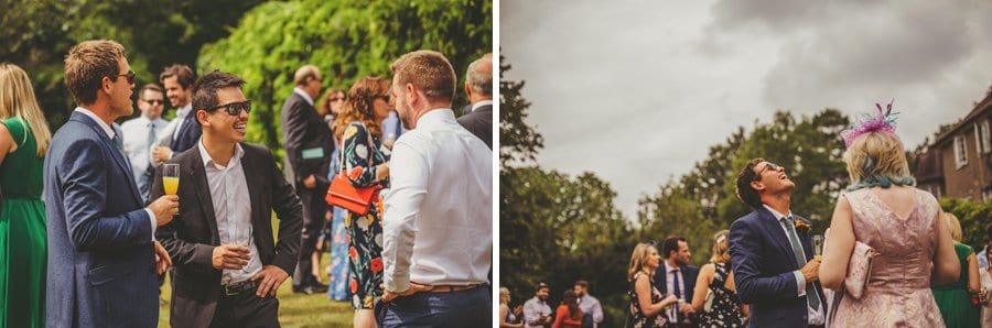 Wedding guests drinking champagne laugh and joke with one another on the lawn at the back of Barley Wood house