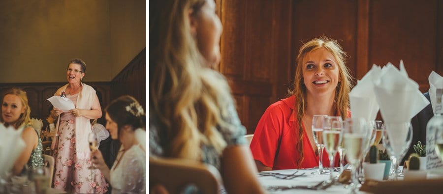 The brides mother stands up and delivers her speech and the grooms sister sits at a table and smiles