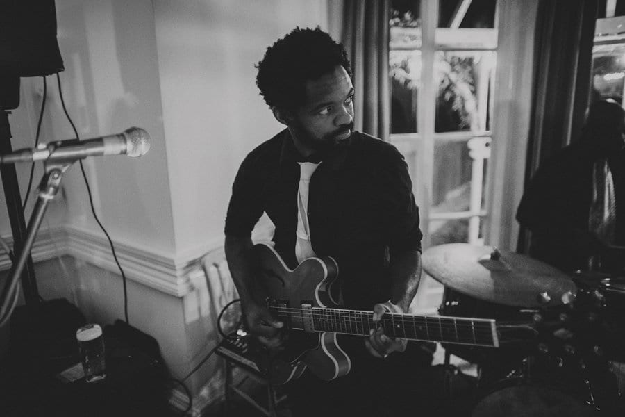 The guitarist of the band playing his guitar and looking at the drummer