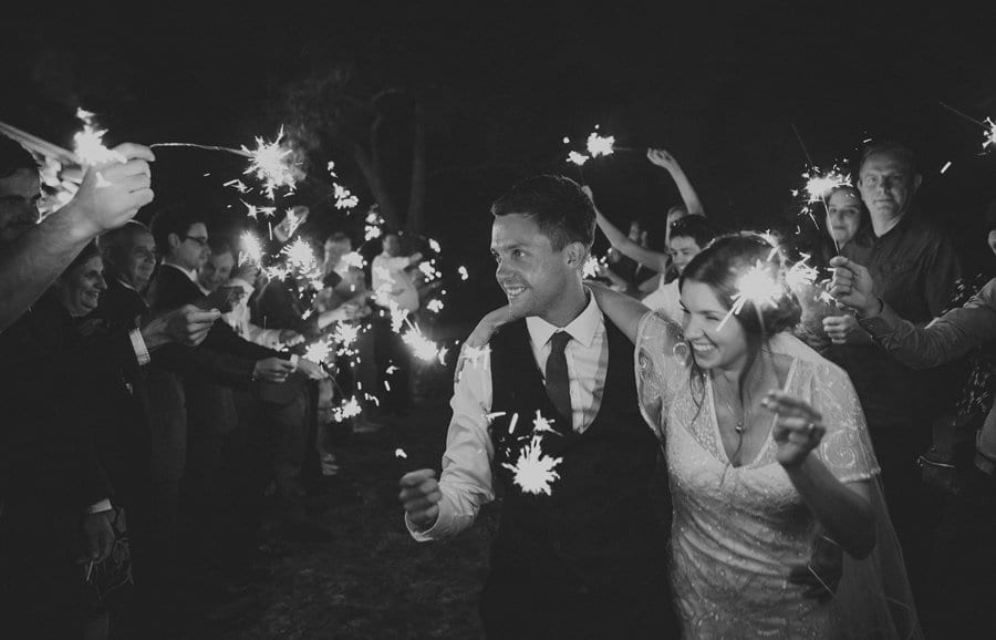 The bride and groom walk along in between the wedding guests and everybody holds sparklers together up in the air