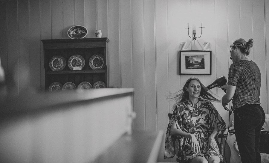 The hairdresser blow dries the brides hair as she sits in a chair