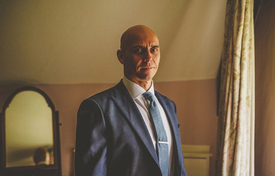 The groom poses for a photograph in one of the bedrooms at Abbey House Gardens