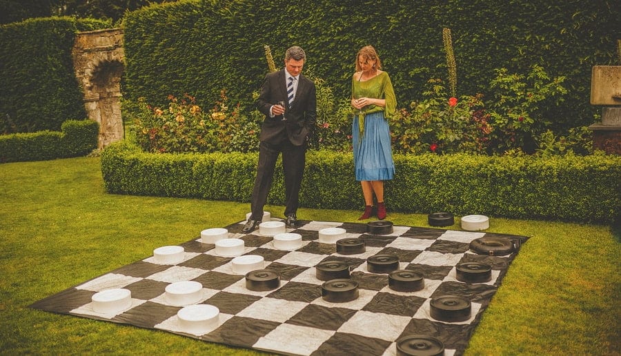 Two wedding guests look at a large draughts board on the grass at Abbey House Gardens