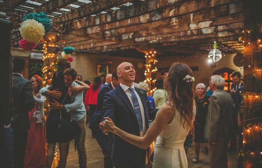 The groom holds his brides hands on the dancefloor and smiles at her