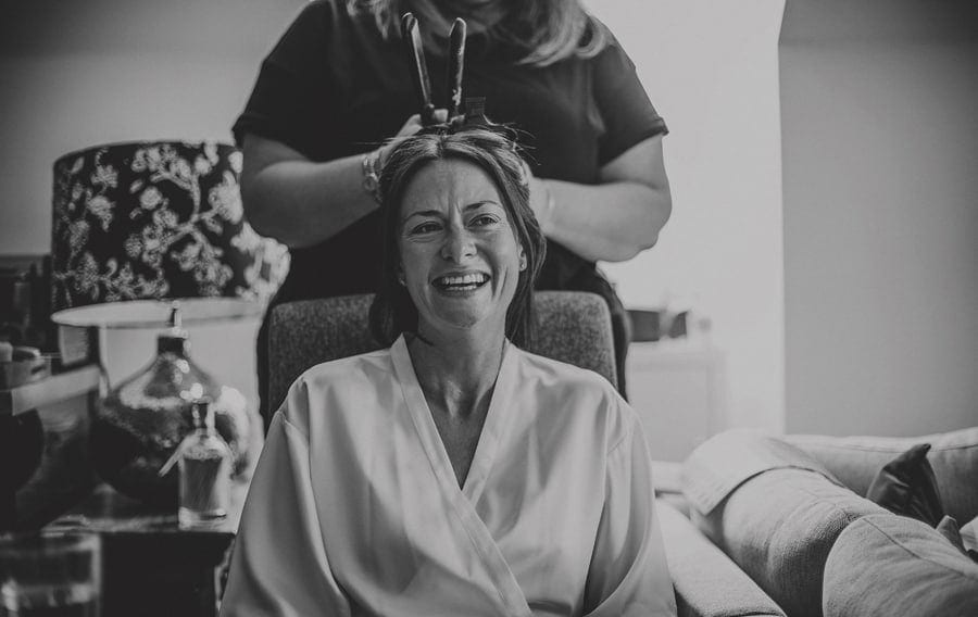 The bride laughs as her hairdresser ties her hair back