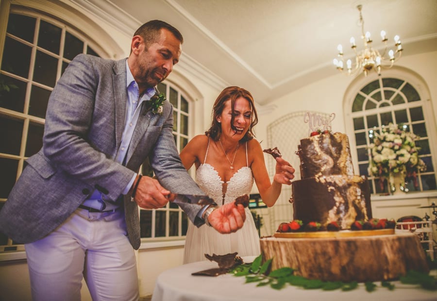 The bride picks up chocolate from the table as her husband cuts the cake