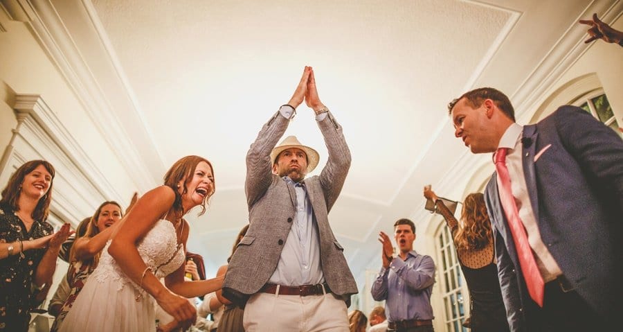 The groom puts his arms in the air as the wedding guests watch on the dancefloor
