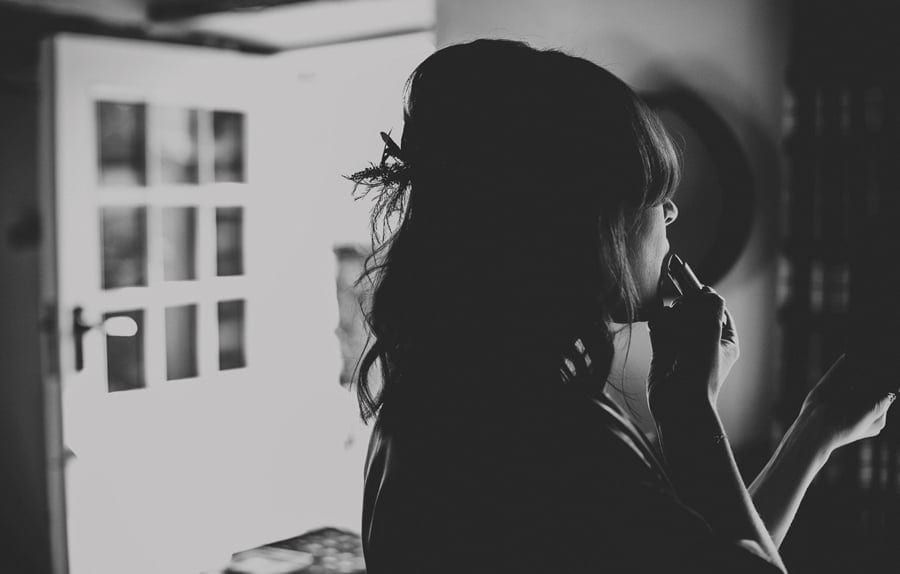 A bridesmaid puts on lipstick in the kitchen of the cottage