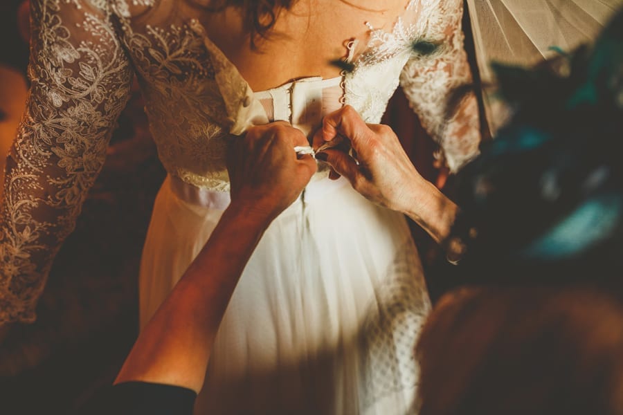 The mother of the bride ties the back of her daughters wedding dress in one of the bedrooms of the cottage