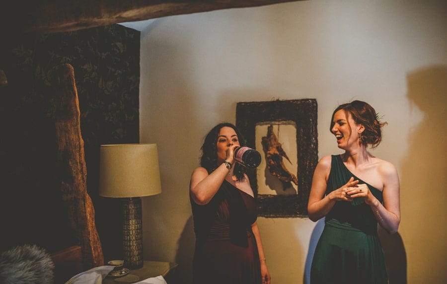 A bridesmaid puts a bottle of champagne to her mouth as her friend standing next to her laughs