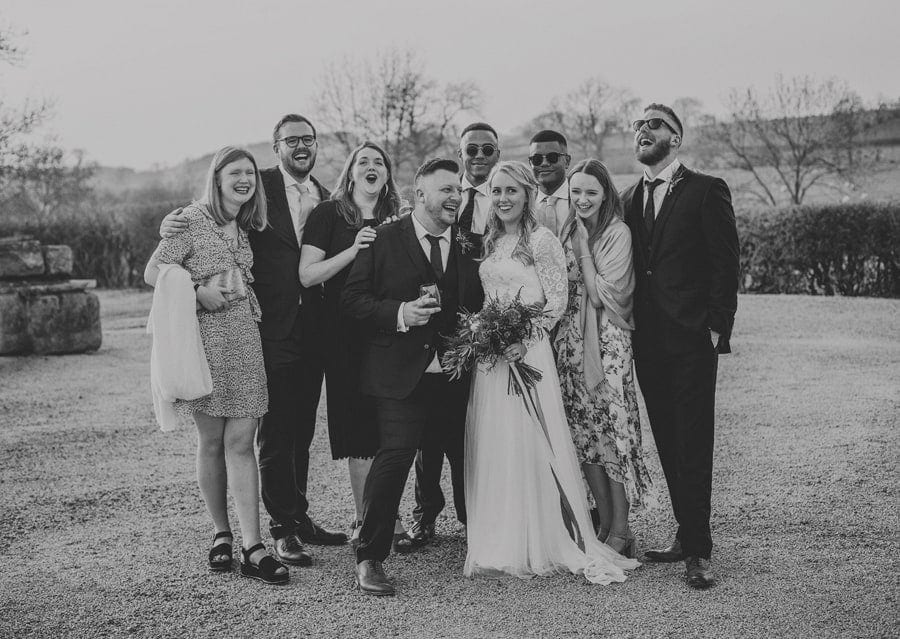 The bride and groom pose for a photograph with friends and family in the courtyard at Eden Barn