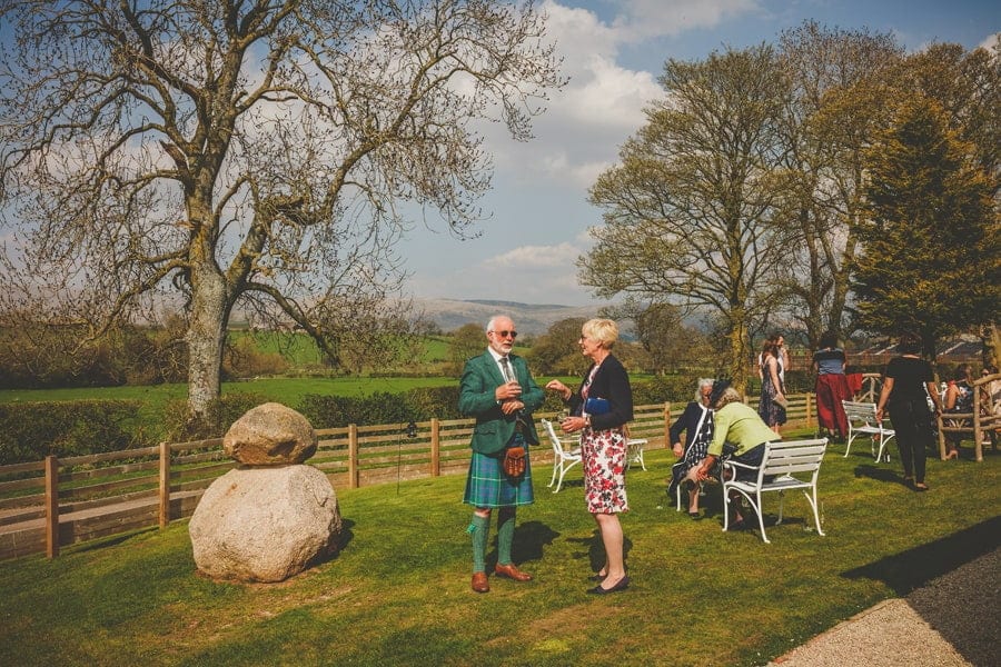 Wedding guests drink champagne and chat to one another in the garden at Eden Barn