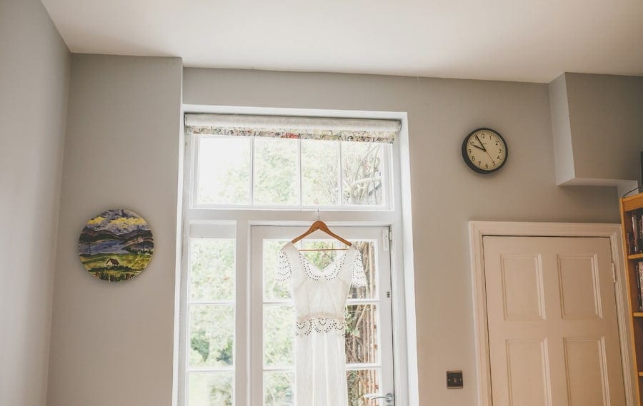The brides dress hangs from a window ledge in the kitchen of the brides house