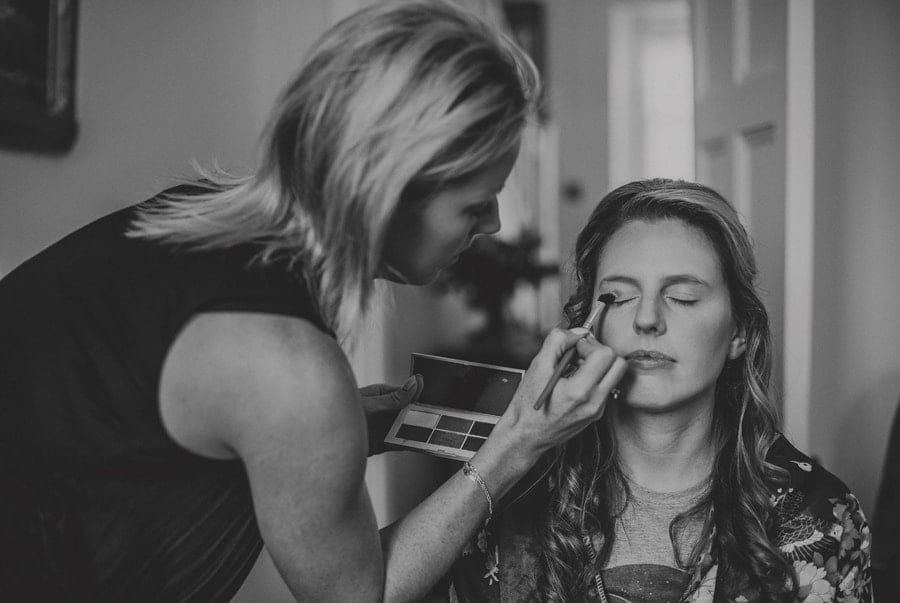 The makeup artist applies make up to a bridesmaid sat on a chair