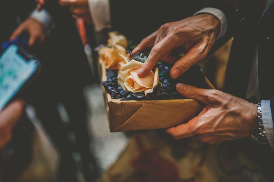 An usher holds a box and puts his finger on a rose