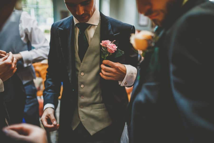 The groom places a flower on the breast pocket of his suit