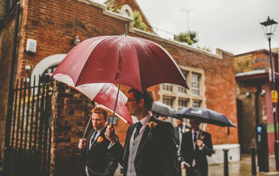 The ushers and the groom hold umbrellas and walk towards the Church
