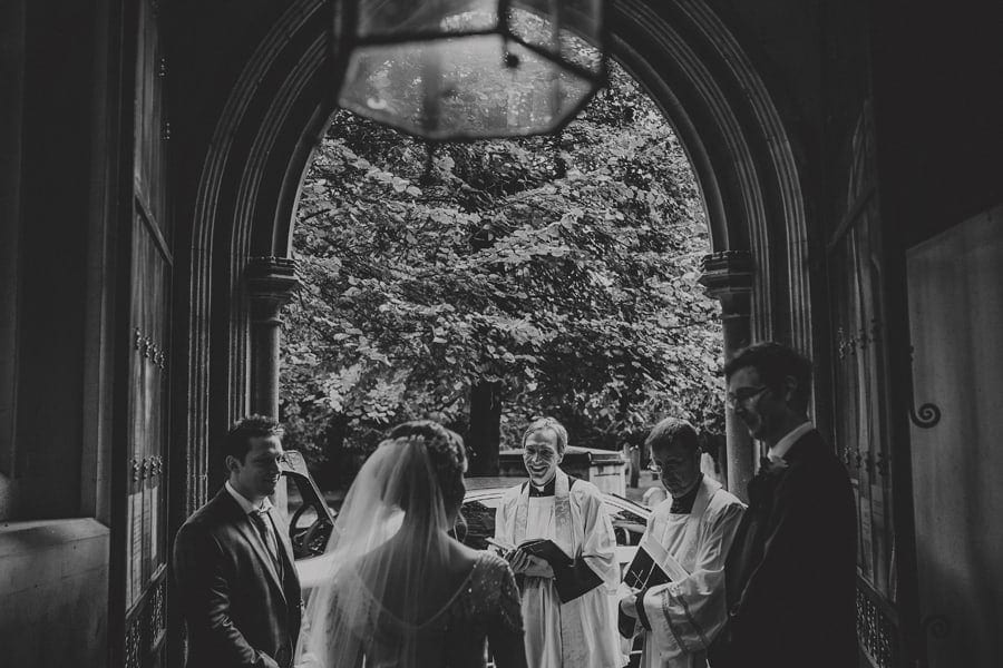 The bride stands at the doorway of the Church and talks to the bridesmaids and the vicar