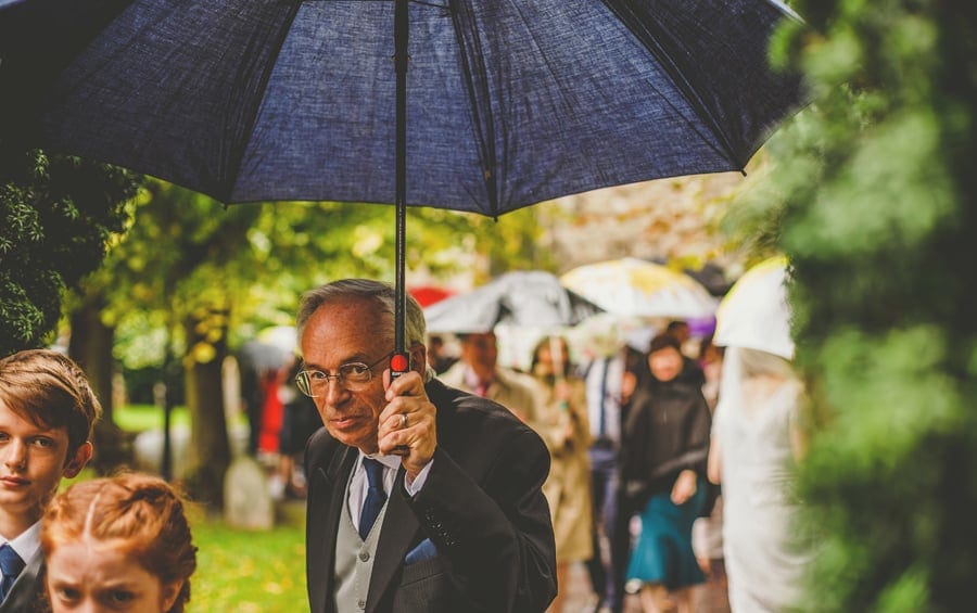 A wedding guest holds an umbrella and walks through the gardens of the Church