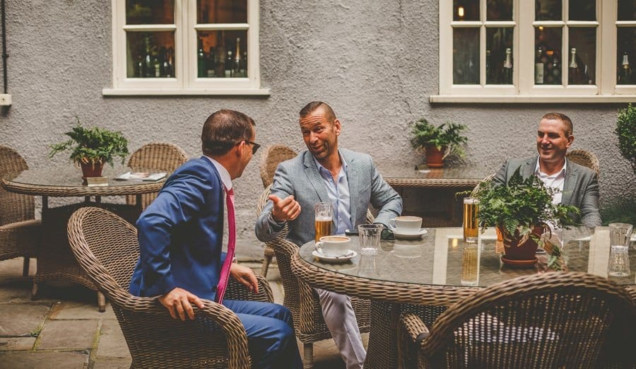 The groom and his ushers sit outside a cafe and chat to one another