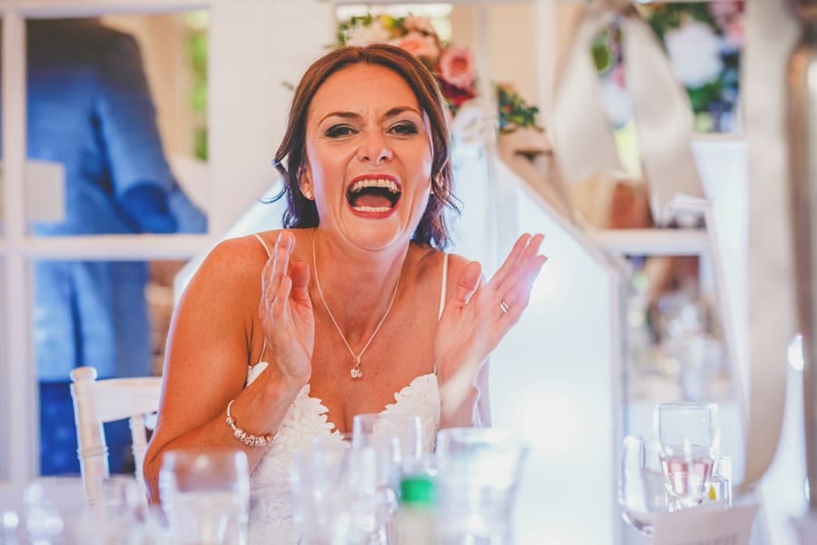 The bride claps her hands and laughs at her husband's wedding speech