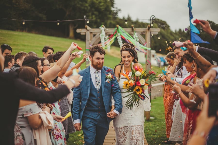 The bride and groom walk into Hadsham Farm as wedding guests throw confetti over them