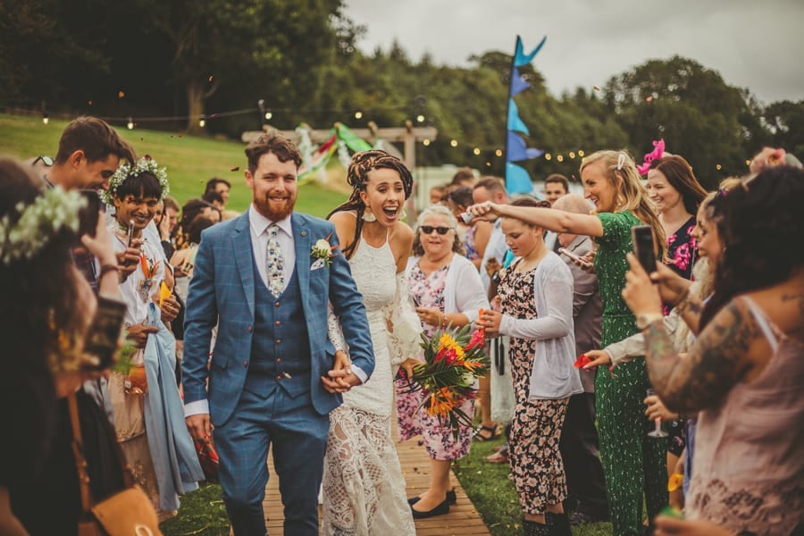 The bride is startled when she is covered in confetti holding the grooms hand at Hadsham Farm