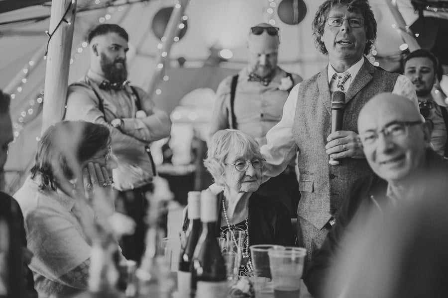 The groom's father puts his arm around his mother and talks to wedding guest during the speech