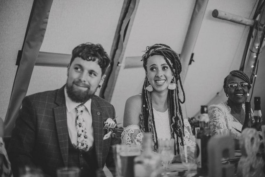The bride and groom listen to the father of the grooms speech in the tipi