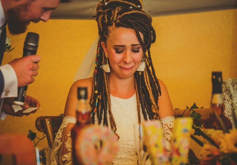 The bride cries as the groom stands over her with a microphone