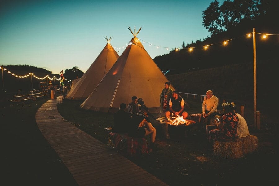 Wedding guests sit around an open fire outside the tipi at Hadsham Farm