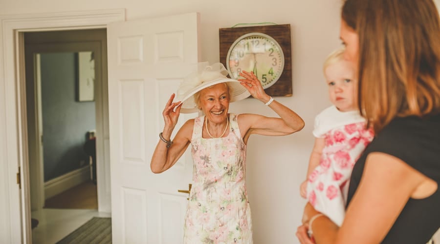 The grooms mother straightens her hat and smiles at her daughter and granddaughter in the kitchen
