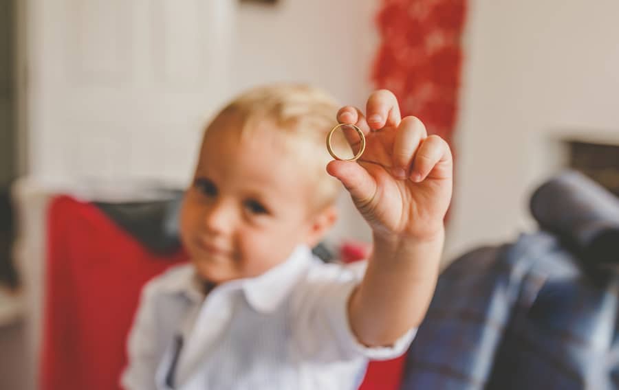 The grooms nephew holds a wedding ring up in the air and poses for a photograph