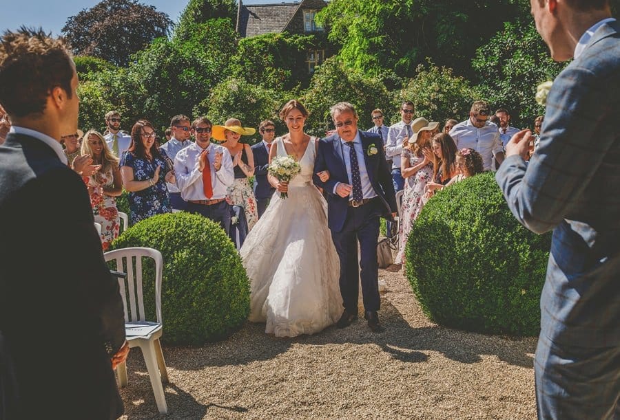 The bride and her father walk towards the groom for the outdoor ceremony at Hanham Court