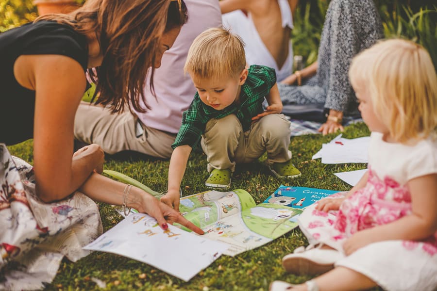 A little boy reads a book with his mother on the grass at Hanham Court