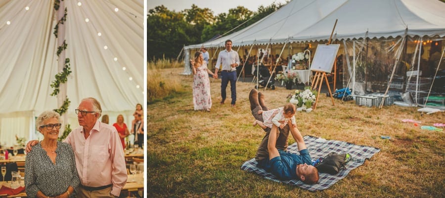 A wedding guest lies on a picnic rug and lifts his daughter in the air next to the marquee at Hanham Court